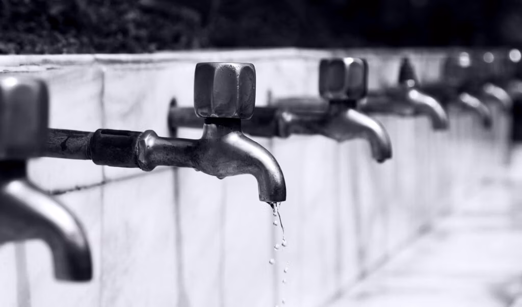 Frequently Asked Questions Black and white image of a row of faucets with water dripping, highlighting plumbing details.