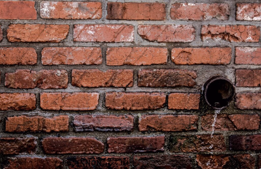 Frequently Asked Questions Close-up of a red brick wall with water flowing from a drain, showcasing texture and patterns.