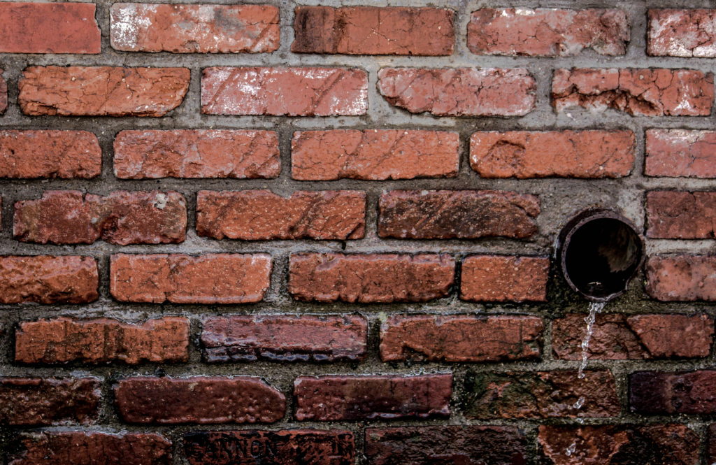 Close-up of a red brick wall with water flowing from a drain, showcasing texture and patterns.