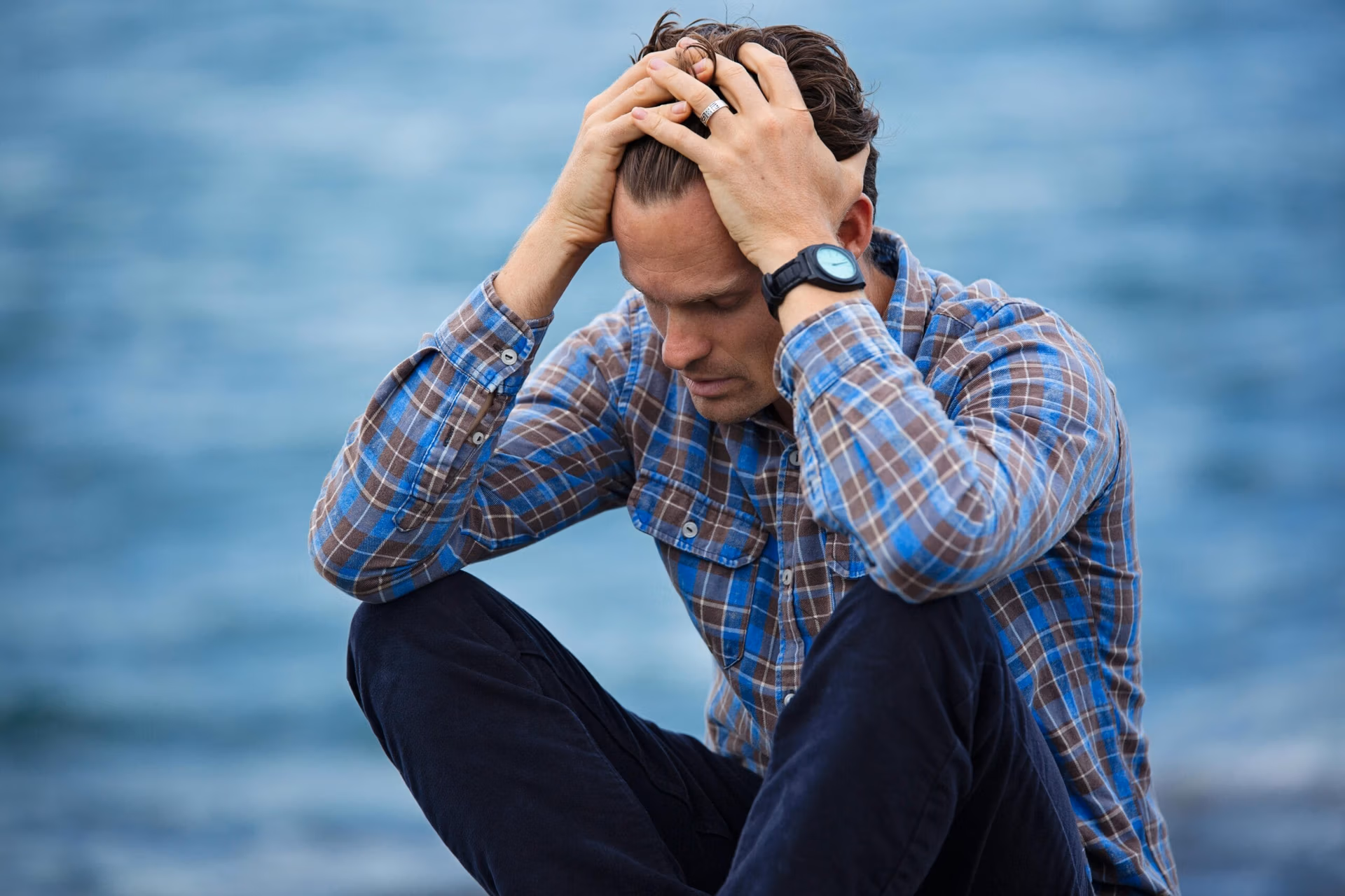 Why Choose Us A man in a plaid shirt sits by the water looking distressed, symbolizing stress.